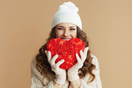 Téléchargez les photos : Hello winter. happy elegant female in beige sweater, mittens and hat against beige background with red heart. - en image libre de droit