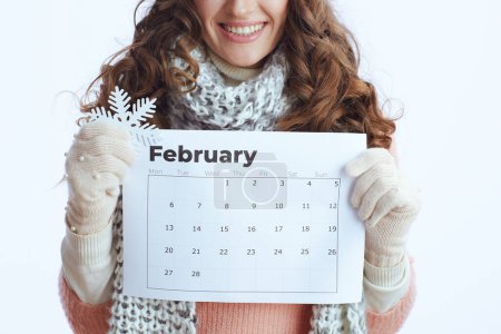 Photo for Hello winter. Closeup on modern 40 years old woman in sweater, mittens, hat and scarf with february calendar and snowflake isolated on white. - Royalty Free Image
