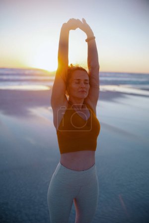 Photo for Relaxed active sports woman in sport clothes at the beach at sunset stretching. - Royalty Free Image