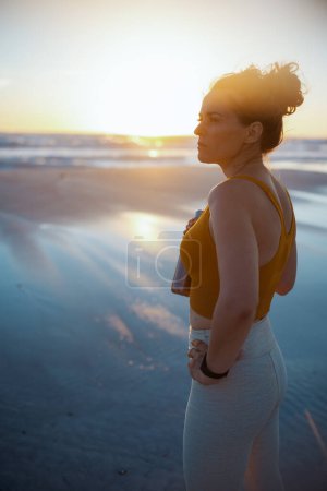 Téléchargez les photos : Fit sports woman in fitness clothes with bottle of water at the beach in the evening. - en image libre de droit