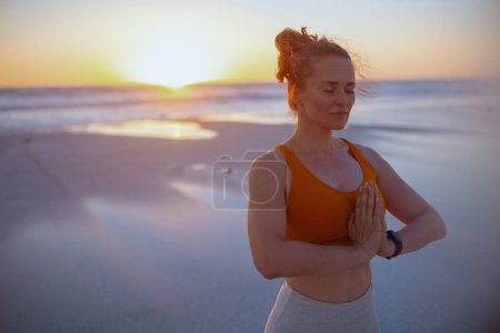 Photo for Fitness sports woman in fitness clothes at the beach at sunset meditating. - Royalty Free Image