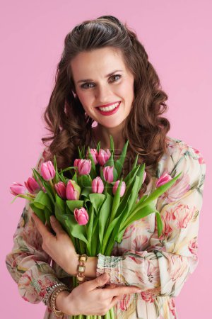 Foto de Happy stylish woman in floral dress with tulips bouquet isolated on pink. - Imagen libre de derechos
