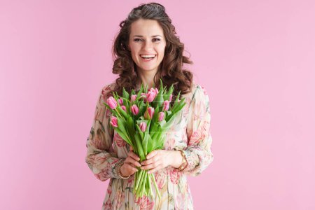 Photo for Happy modern middle aged woman in floral dress with tulips bouquet isolated on pink. - Royalty Free Image