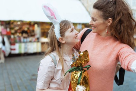 Foto de Easter fun. smiling modern mother and child with golden easter egg at the fair in the city. - Imagen libre de derechos
