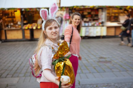 Photo for Easter fun. smiling young mother and teenage daughter with golden easter egg walking at the fair in the city. - Royalty Free Image