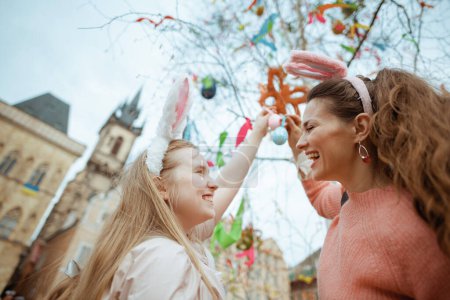 Téléchargez les photos : Easter fun. happy modern mother and teenage daughter with easter eggs in the front of easter decorated tree at the fair in the city. - en image libre de droit