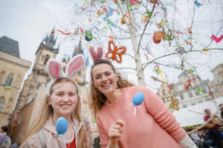 Easter fun. Portrait of happy young mother and teenage daughter with easter eggs in the front of easter decorated tree at the fair in the city.