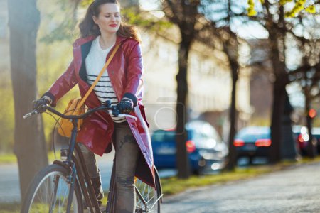 Téléchargez les photos : Relaxed modern woman in red rain coat outside on the city street riding bicycle. - en image libre de droit