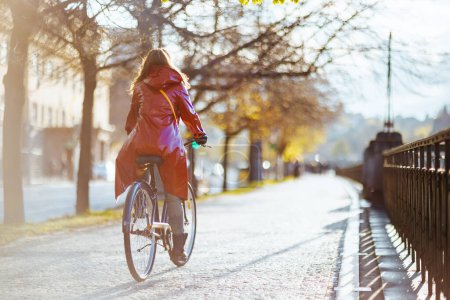 Foto de Seen from behind woman in red rain coat outdoors in the city riding bicycle. - Imagen libre de derechos