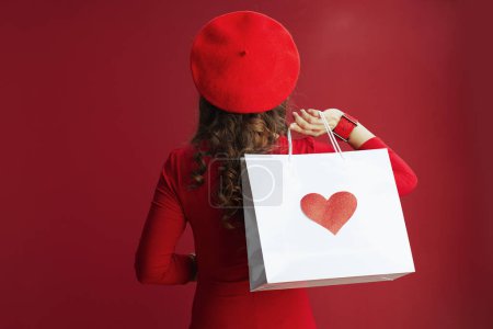 Photo for Happy Valentine. Closeup on middle aged woman in red dress and beret with shopping bag with heart isolated on red. - Royalty Free Image