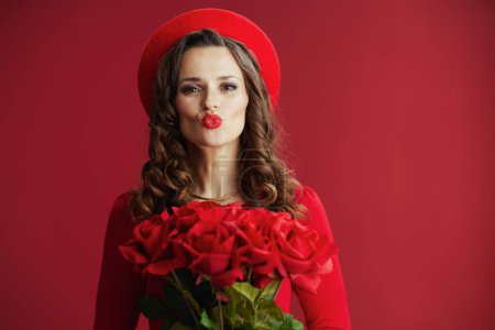 Happy Valentine. modern woman in red dress and beret isolated on red background with red roses sending a kiss.