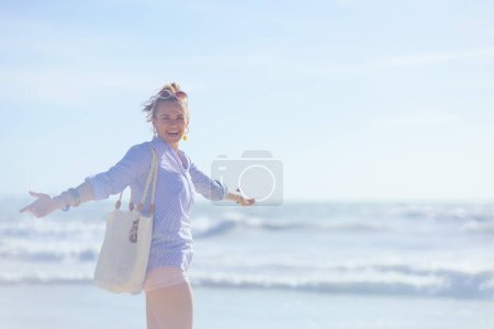 Téléchargez les photos : Smiling stylish woman with white straw bag rejoicing at the beach. - en image libre de droit