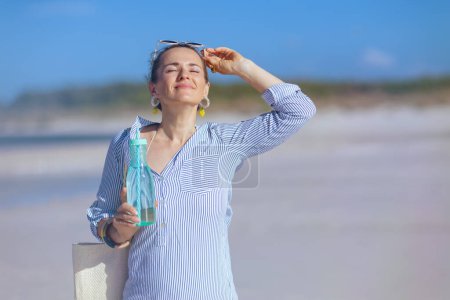 Foto de Relaxed modern female with white straw bag and drink at the beach. - Imagen libre de derechos