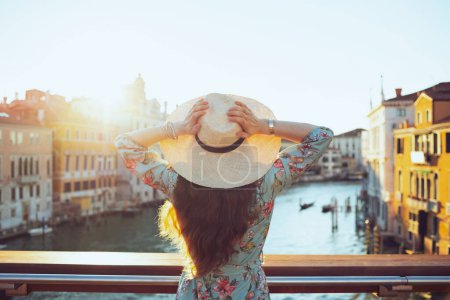 Foto de Visto desde atrás mujer joven en vestido floral con sombrero en el puente de la Academia en Venecia, Italia. - Imagen libre de derechos