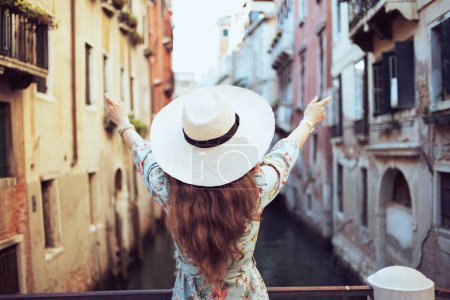 Foto de Visto desde atrás Mujer viajera de mediana edad en vestido floral con sombrero en Venecia, Italia. - Imagen libre de derechos