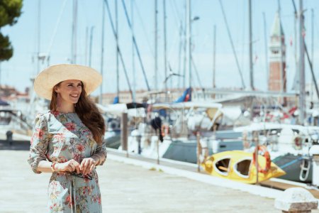 Foto de Happy young tourist woman in floral dress with sunglasses and hat on the pier. - Imagen libre de derechos