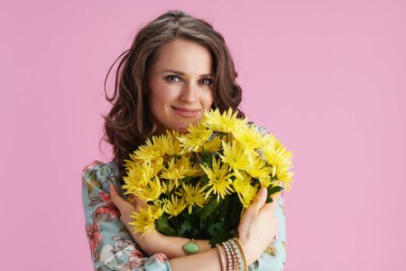 Foto de Happy young woman with long wavy brunette hair with yellow chrysanthemums flowers against pink background. - Imagen libre de derechos