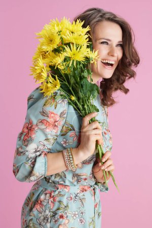 Photo for Happy modern middle aged woman in floral dress with yellow chrysanthemums flowers isolated on pink background. - Royalty Free Image
