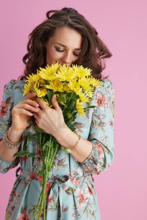 Photo for Relaxed middle aged woman in floral dress with yellow chrysanthemums flowers isolated on pink background. - Royalty Free Image