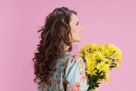 Photo for Smiling young woman in floral dress with yellow chrysanthemums flowers isolated on pink. - Royalty Free Image