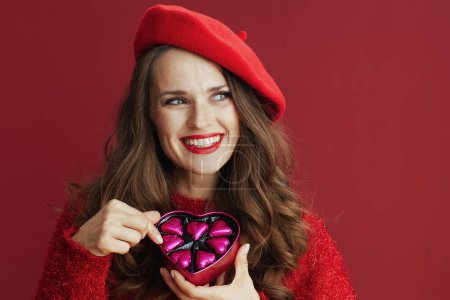 Foto de Happy Valentine. smiling elegant middle aged woman in red sweater and beret with heart shaped candy box. - Imagen libre de derechos