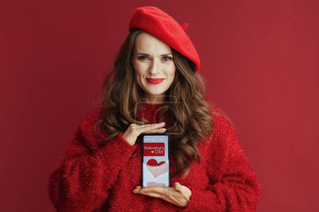 Photo for Happy Valentine. happy elegant 40 years old woman with long wavy hair in red sweater and beret , smartphone and Valentine app. - Royalty Free Image