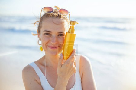 Foto de Portrait of happy stylish female in white swimwear at the beach applying sunscreen. - Imagen libre de derechos