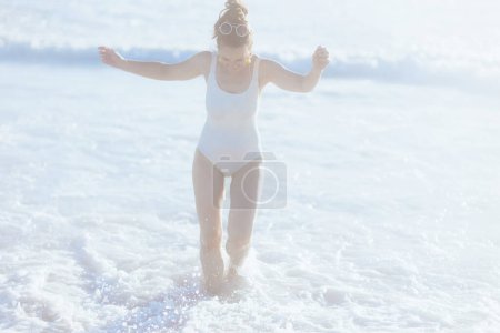 Téléchargez les photos : Full length portrait of smiling modern 40 years old woman in white swimwear at the beach having fun time. - en image libre de droit