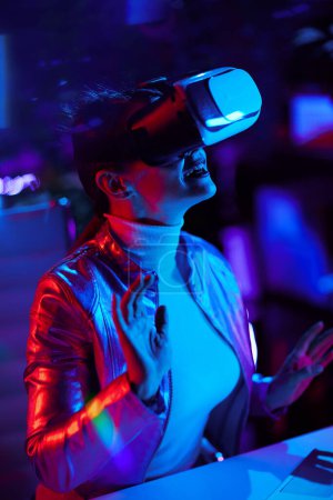 Photo for Neon metaverse futuristic concept. smiling stylish woman in vr headset exploring metaverse in modern office. - Royalty Free Image
