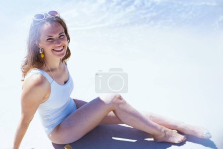 Foto de Happy modern 40 years old woman in white beachwear sitting at the beach. - Imagen libre de derechos