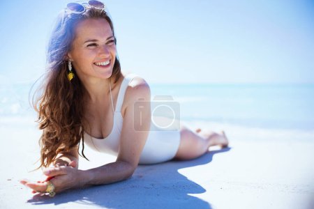 Foto de Smiling stylish middle aged woman in white swimwear laying at the beach. - Imagen libre de derechos