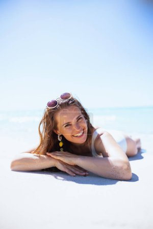 lächelnde moderne 40-jährige Frau am Strand liegend.