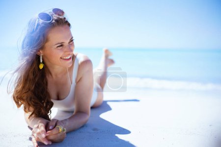 Téléchargez les photos : Happy elegant female in white swimsuit laying at the beach. - en image libre de droit