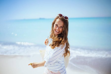 Photo for Portrait of smiling modern 40 years old woman at the beach in white striped shirt and shorts having fun time. - Royalty Free Image