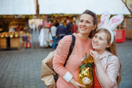 Foto de Easter fun. smiling modern mother and child with golden easter egg at the fair in the city. - Imagen libre de derechos