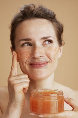 Foto de Happy middle aged woman with face scrub on beige background. - Imagen libre de derechos