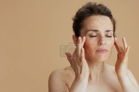 Foto de Young woman with face scrub isolated on beige. - Imagen libre de derechos