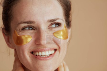 Téléchargez les photos : Smiling middle aged woman with eye patches on beige background. - en image libre de droit