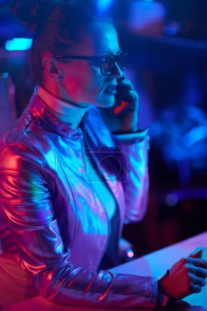 Photo for Neon metaverse futuristic concept. stylish woman in glasses speaking on a smartphone in modern office. - Royalty Free Image