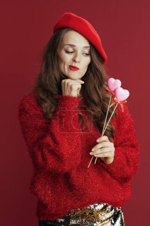 Foto de Happy Valentine. modern woman with long wavy hair in red sweater and beret and hearts on stick. - Imagen libre de derechos