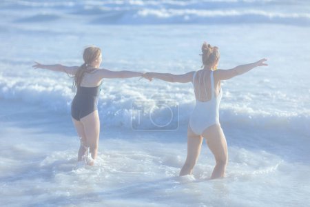 Téléchargez les photos : Vu de derrière la mère et l'enfant élégants à la plage en maillot de bain avoir du plaisir. - en image libre de droit