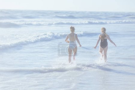 Téléchargez les photos : Seen from behind stylish mother and child at the beach in beachwear running. - en image libre de droit