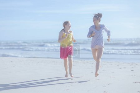 Photo for Full length portrait of smiling modern mother and teenage daughter at the beach running. - Royalty Free Image