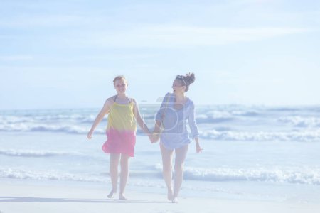 Téléchargez les photos : Full length portrait of smiling modern mother and teenage daughter at the beach walking. - en image libre de droit