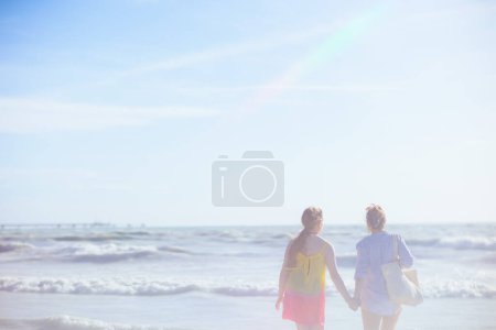 Foto de Seen from behind stylish mother and teenage daughter at the beach relaxing. - Imagen libre de derechos