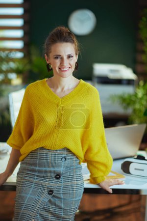 Foto de Smiling elegant small business owner woman in yellow sweater standing in the modern green office. - Imagen libre de derechos