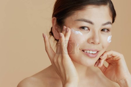 Téléchargez les photos : Portrait of modern asian female with facial cream on face isolated on beige background. - en image libre de droit