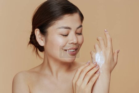 Téléchargez les photos : Young woman with hand cream against beige background. - en image libre de droit