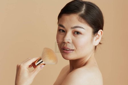 Photo for Portrait of young asian woman with makeup brush isolated on beige background. - Royalty Free Image