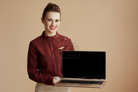 Photo for Happy elegant air hostess woman on beige background showing laptop blank screen. - Royalty Free Image
